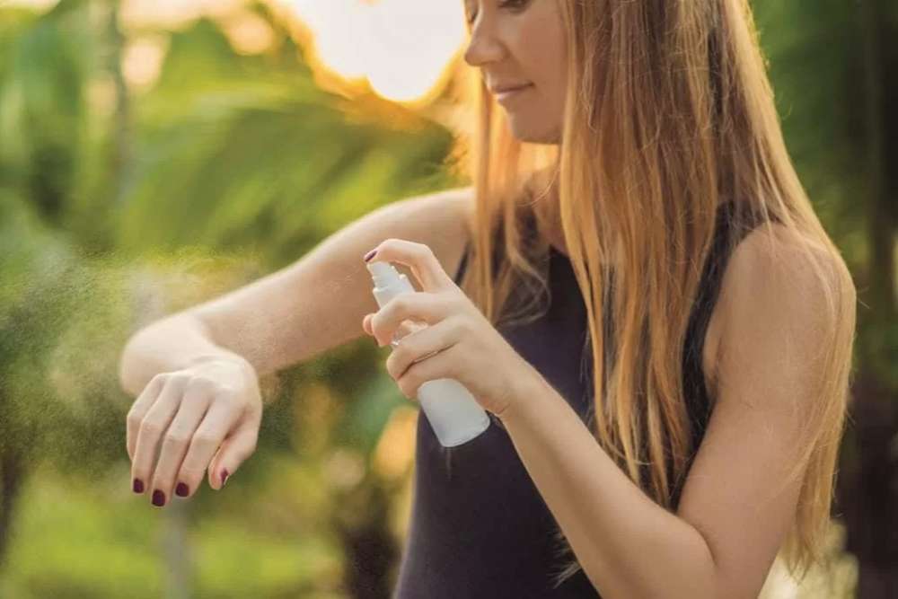 La niña está rociando repelente de mosquitos.